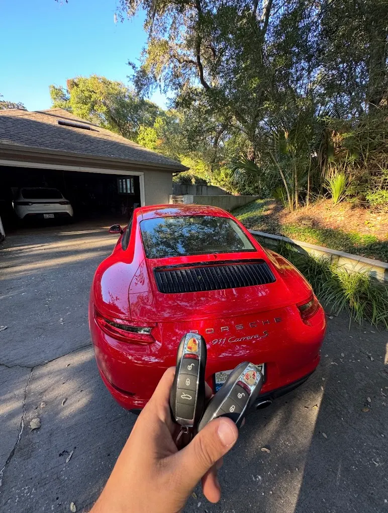 Two new key fobs held up in front of a red Porsche 911