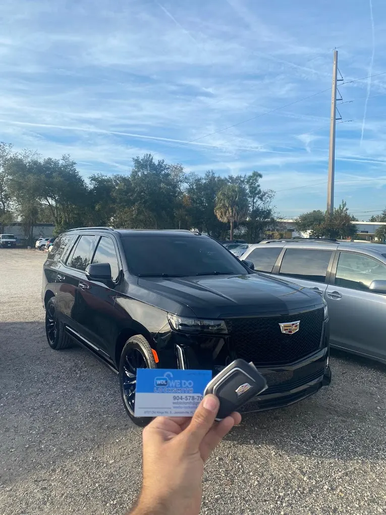 Technician holding a new key fob and the We Do Locksmith business card beside a customer's Cadillac